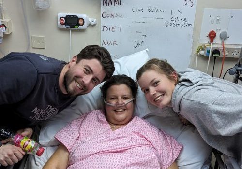 Female in hospital bed with male and female either side of her.