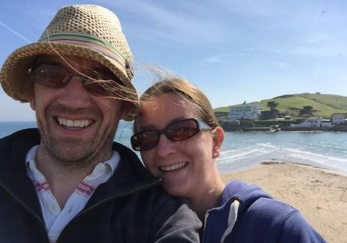 Husband and wife on windy beach, taking a selfie with sea in the background