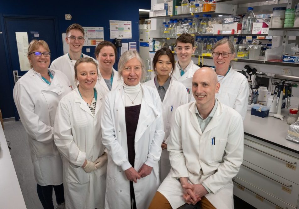 staff and students in a group shot in the lab, all are wearing white lab coats.